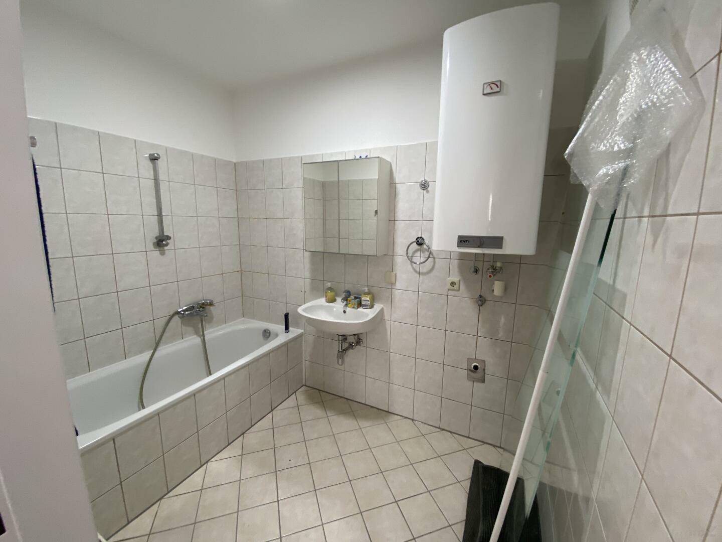 Badezimmer mit Badewanne, Waschbecken, Spiegelschrank und Wandfliesen in hellem Grau.