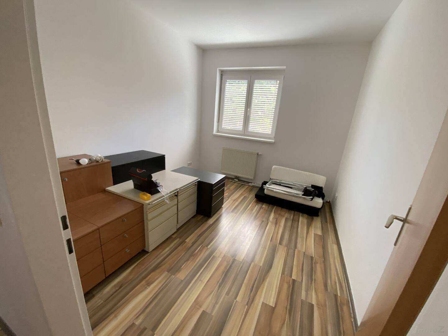 Schlafzimmer mit Laminatboden, Fenster und verschiedenen Möbelstücken, hell und geräumig.