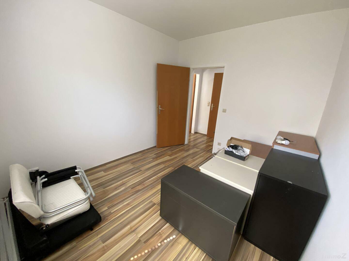 Schlafzimmer mit Laminatboden und Blick in den Flur, derzeit unmöbliert und hell.