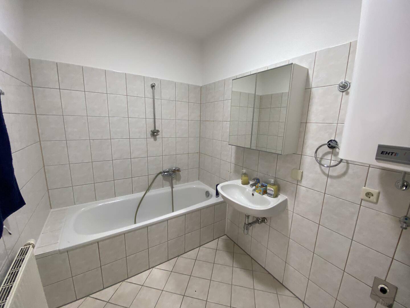 Helles Badezimmer mit Badewanne, Waschbecken und weiß-grauen Wandfliesen, sauber und funktional.