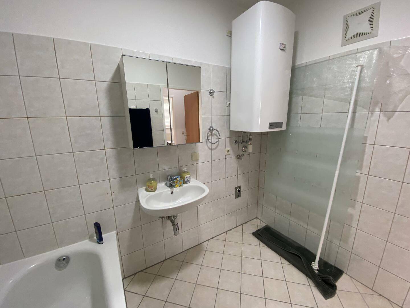 Badezimmer mit Badewanne, Waschbecken, Spiegelschrank und Wandfliesen in hellem Grau.
