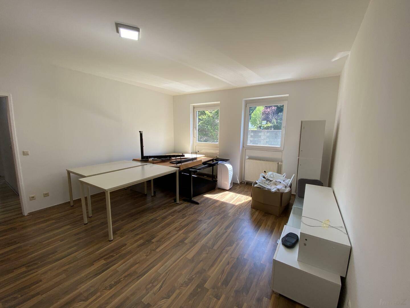 Geräumiges Wohnzimmer mit Laminatboden, zwei Fenstern und viel natürlichem Tageslicht.