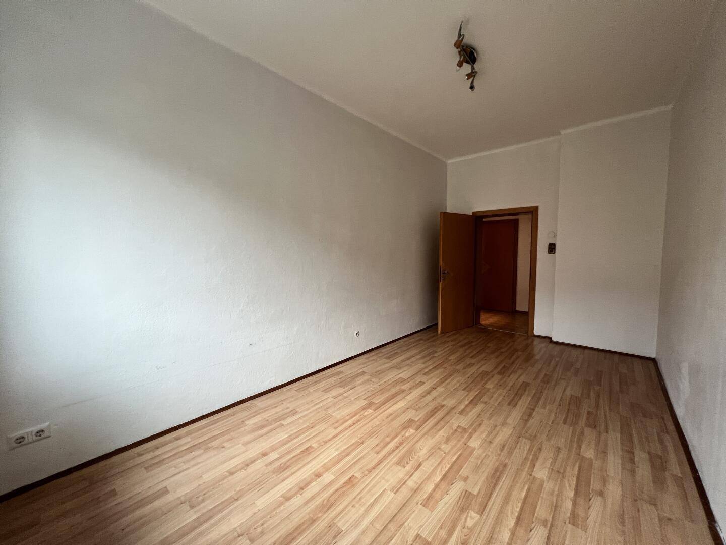 Leeres Zimmer mit hellem Laminatboden und weißen Wänden, bereit für individuelle Gestaltung.