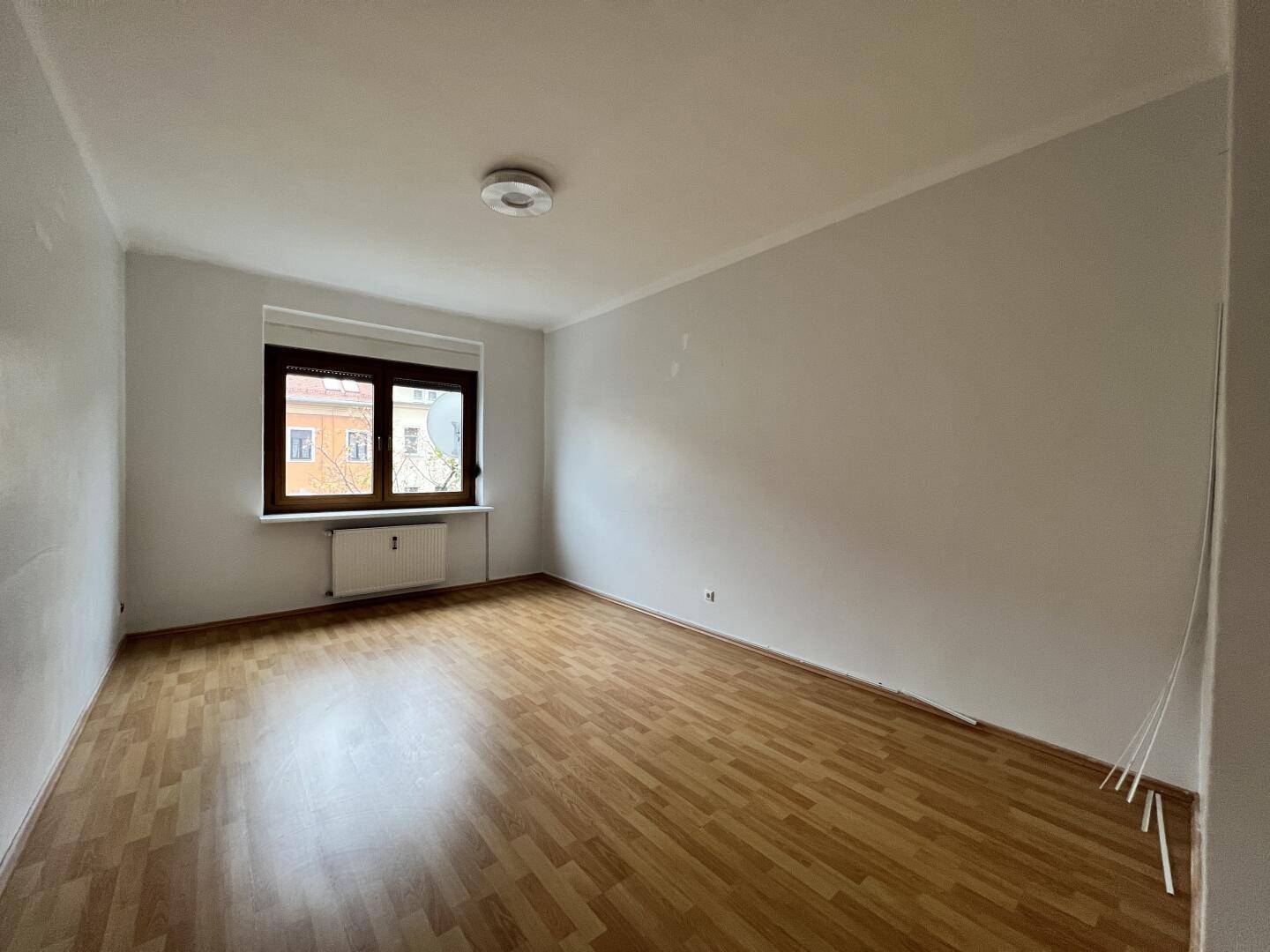Geräumiger, heller Raum mit Laminatboden und einem Fenster, ideal als Wohn- oder Schlafzimmer.