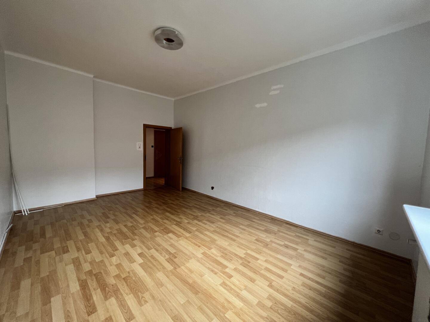 Helles, leeres Zimmer mit Laminatboden und neutralen Wänden, bietet vielseitige Nutzungsmöglichkeiten.