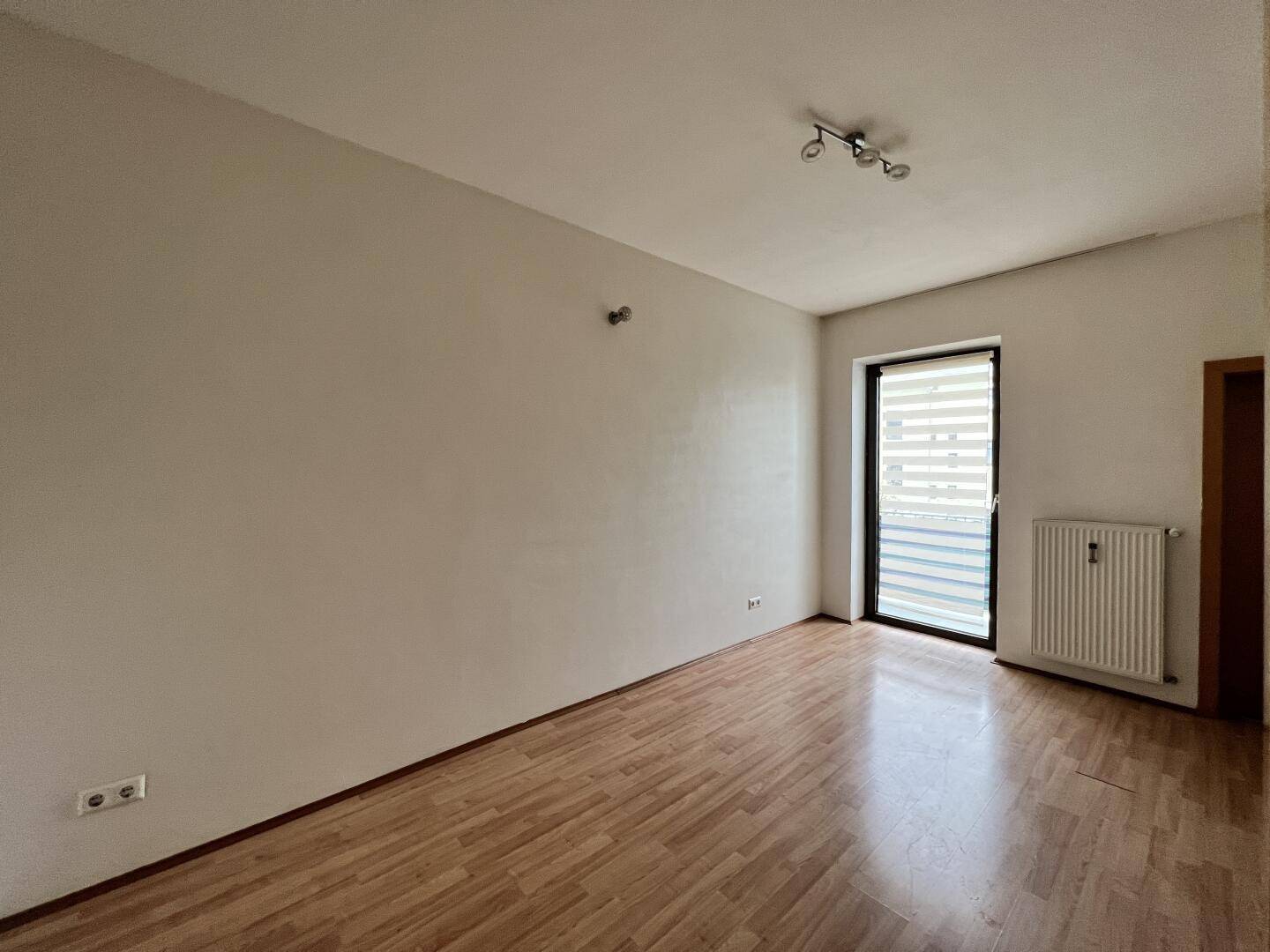 Langer, heller Raum mit Laminatboden und Zugang zu einem möglichen Balkon oder Terrasse.
