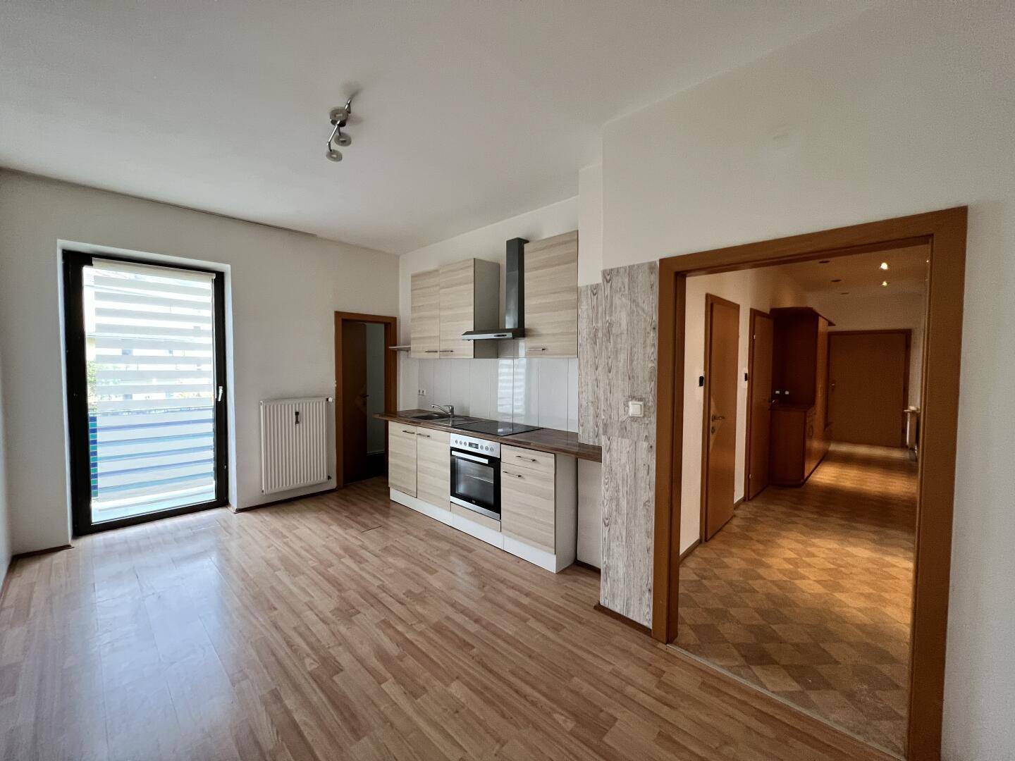 Offener Wohnbereich mit integrierter Küchenzeile und Zugang zum Balkon, ausgestattet mit Laminatboden.