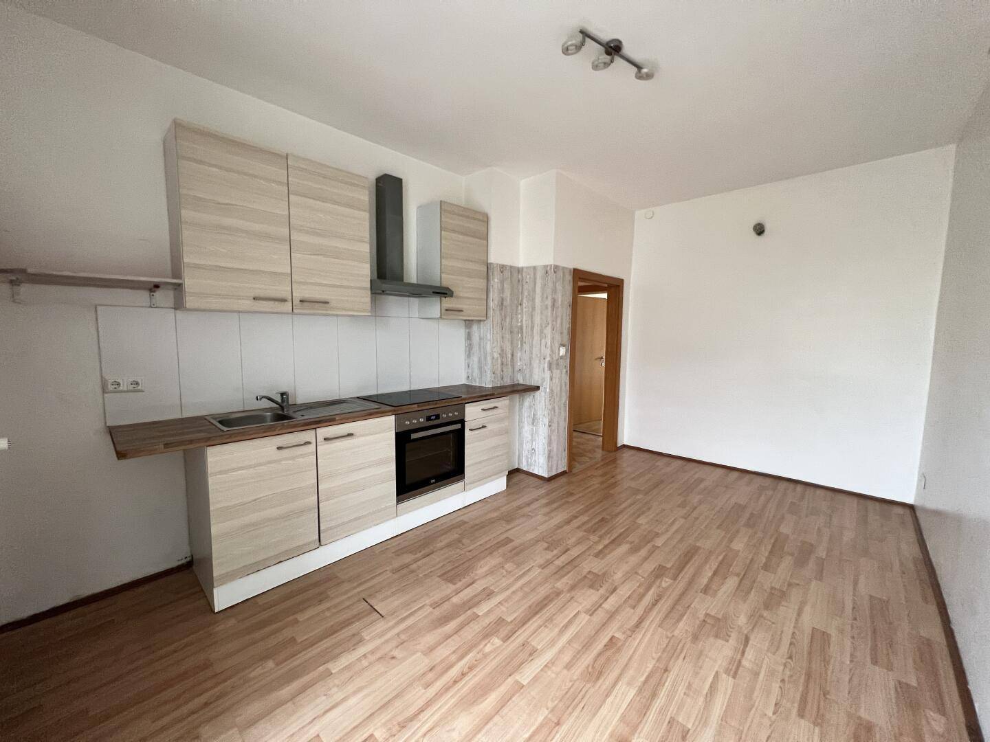 Kleine Einbauküche mit Holzoptik-Fronten und integrierten Geräten in einem offenen Bereich.