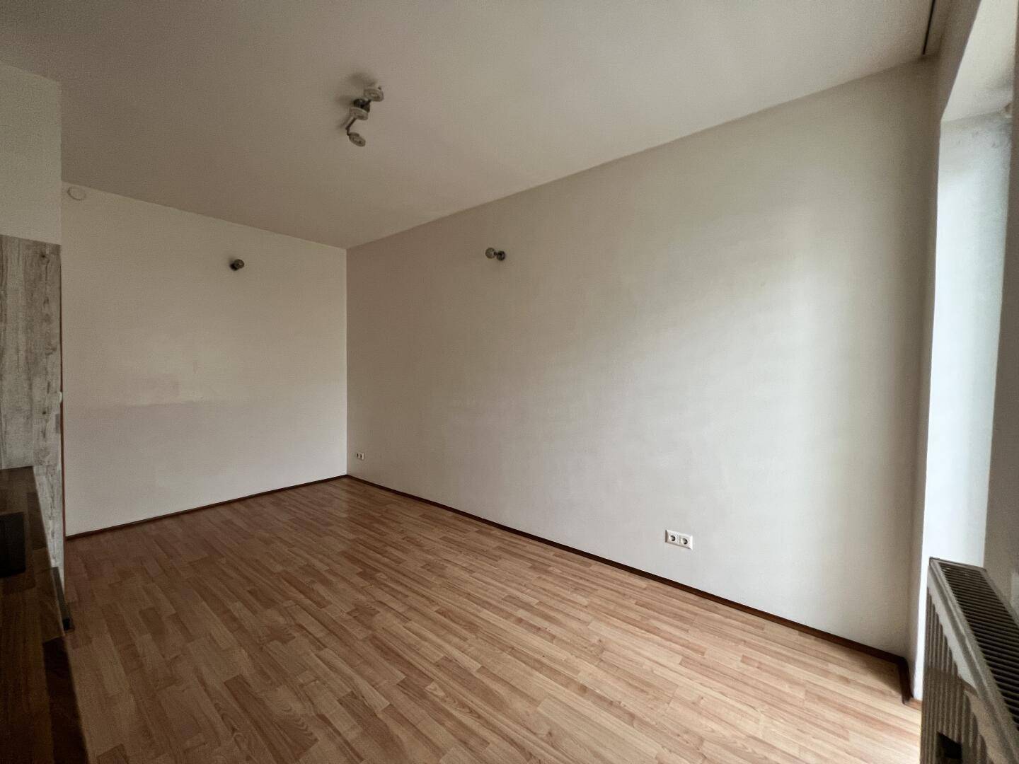 Heller Wohnbereich mit Laminatboden und weißen Wänden, angrenzend an die Küchenzeile.