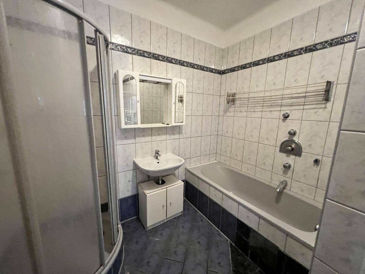 Badezimmer mit Badewanne, Duschkabine und Waschbecken, gefliest in Weiß und Blau.