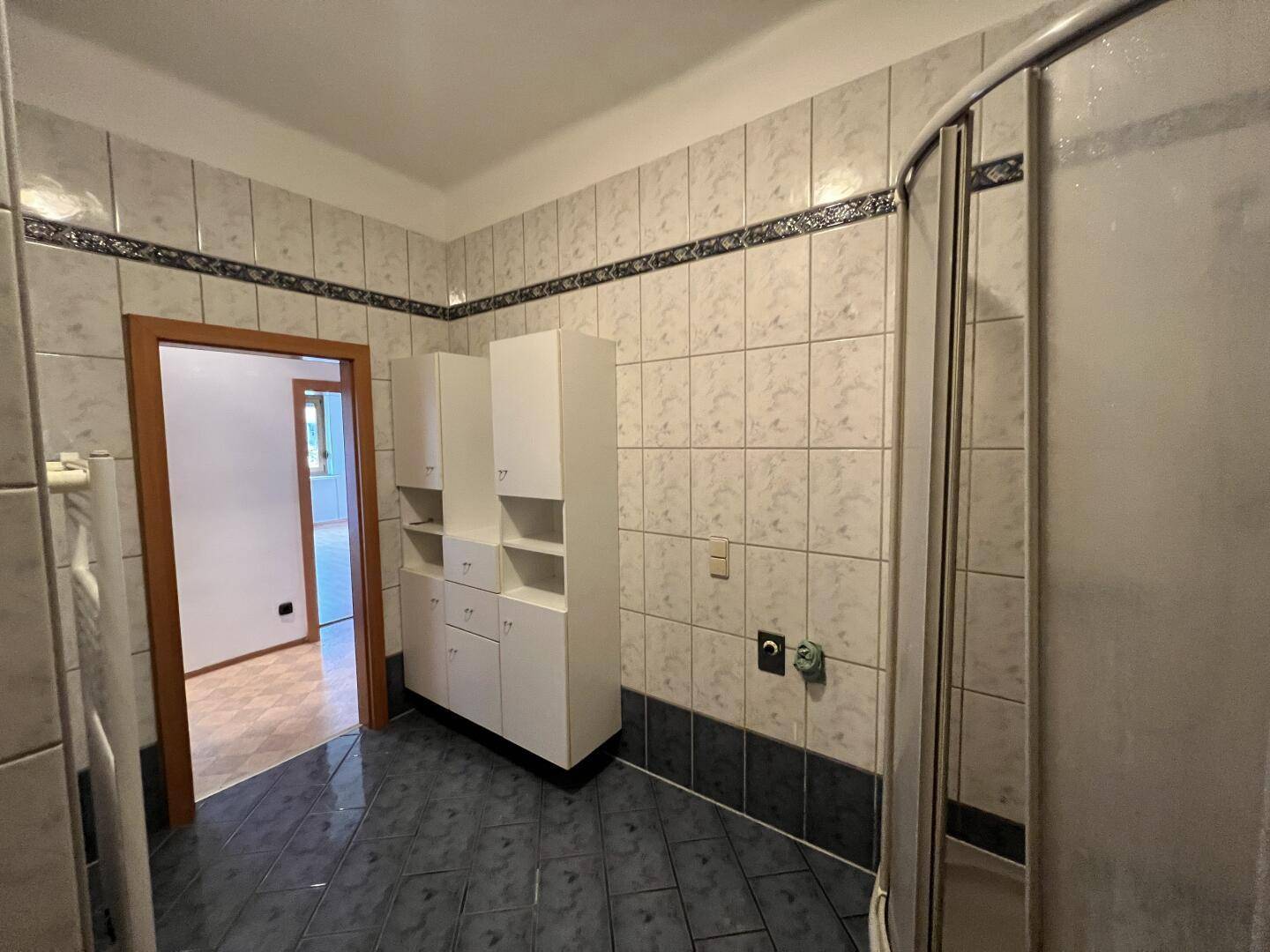 Geräumiges Badezimmer mit Duschkabine und praktischen Hochschränken, gefliest in klassischem Design.