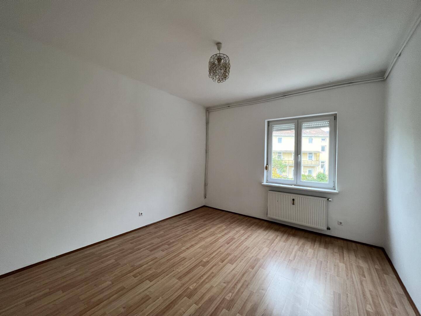 Heller Wohnraum mit Laminatboden und einem Fenster, ausgestattet mit einem Kronleuchter.