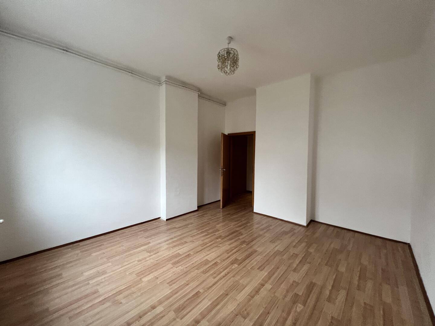 Geräumiges Zimmer mit Laminatboden und neutralen Wänden, ideal als Schlaf- oder Kinderzimmer.