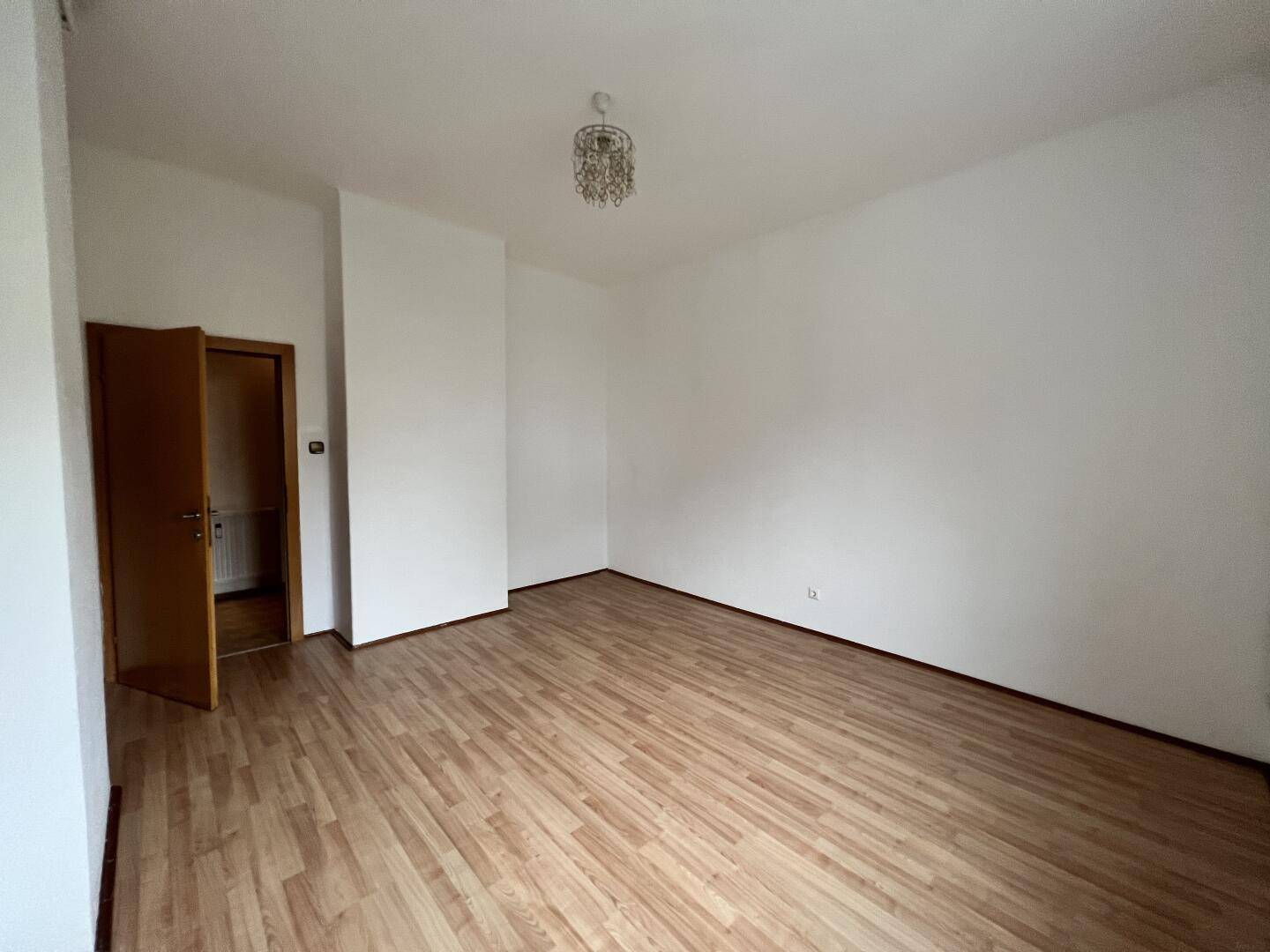 Lichtdurchflutetes Zimmer mit Laminatboden und schlichten weißen Wänden, vielseitig nutzbar.
