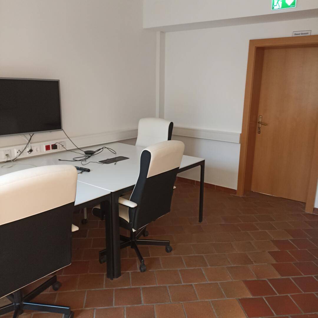 Büro mit Terrakottafliesen, einem großen Bildschirm und mehreren Bürostühlen.