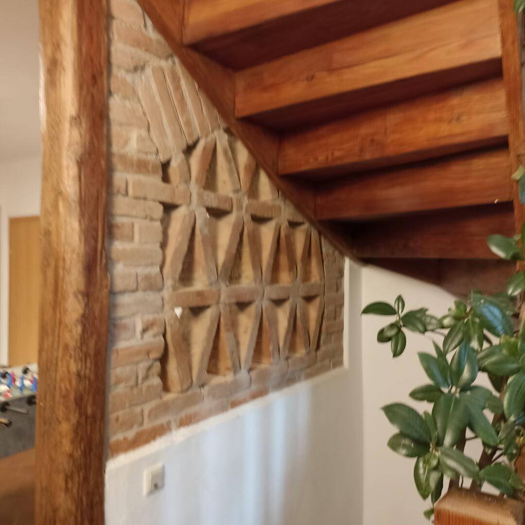 Holztreppe mit Ziegelwand und dekorativen Mustern, die zu den oberen Etagen führt.
