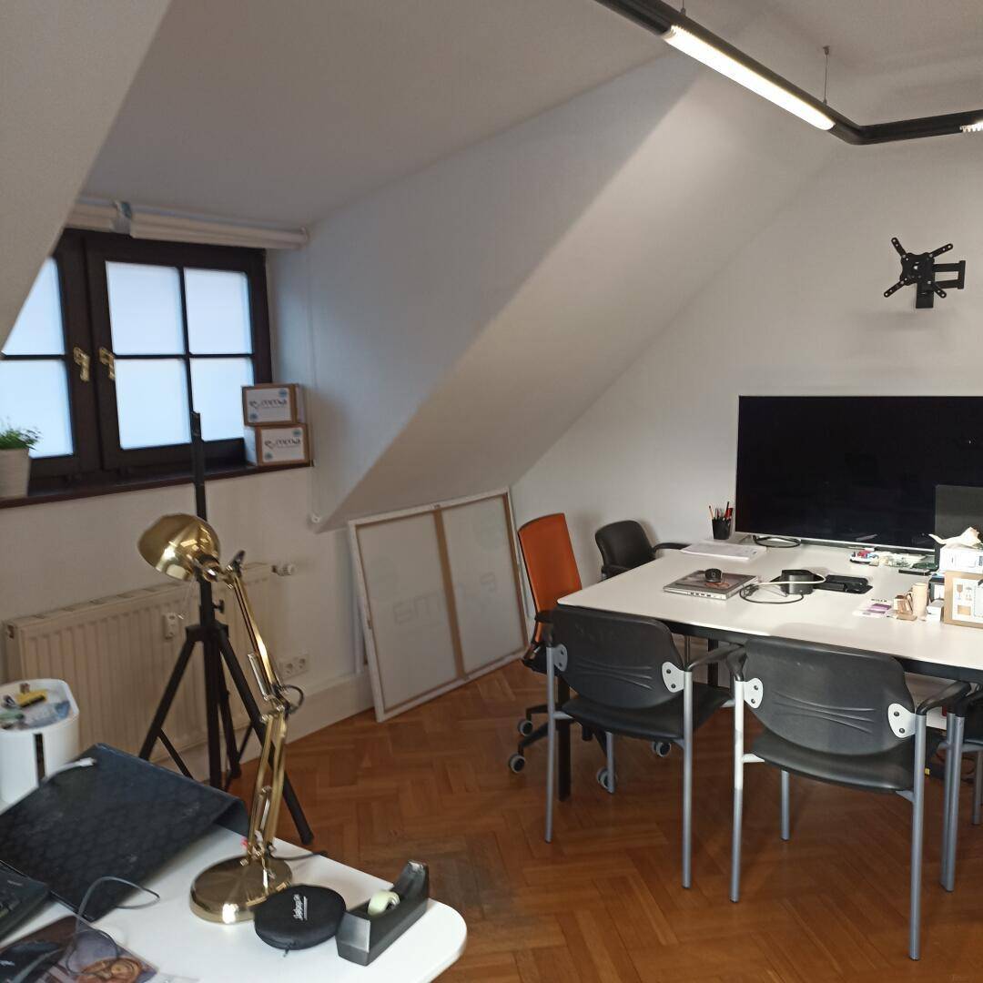 Dachgeschossbüro mit mehreren Arbeitsplätzen, Holzboden und einem großen Fernseher an der Wand.