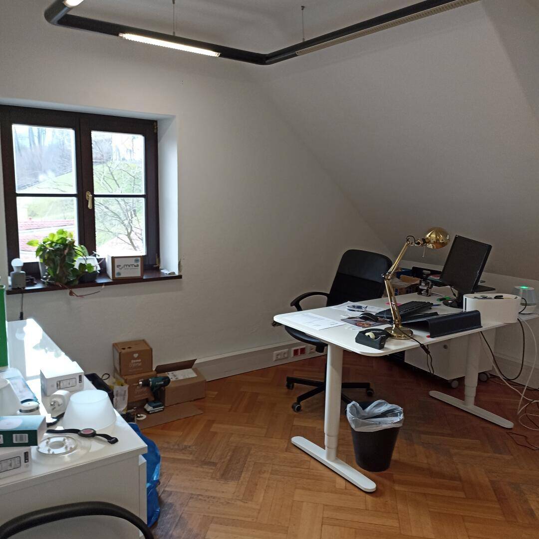 Dachgeschossbüro mit einem Arbeitsplatz, Holzboden und einem Fenster mit Blick nach draußen.