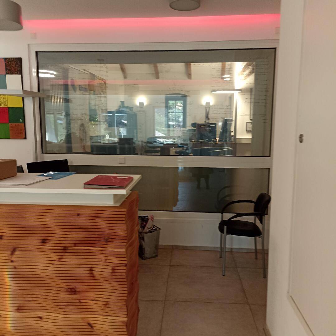 Empfangstheke mit Holzverkleidung und großer Fensterfront, die den Blick in einen weiteren Bürobereich freigibt.