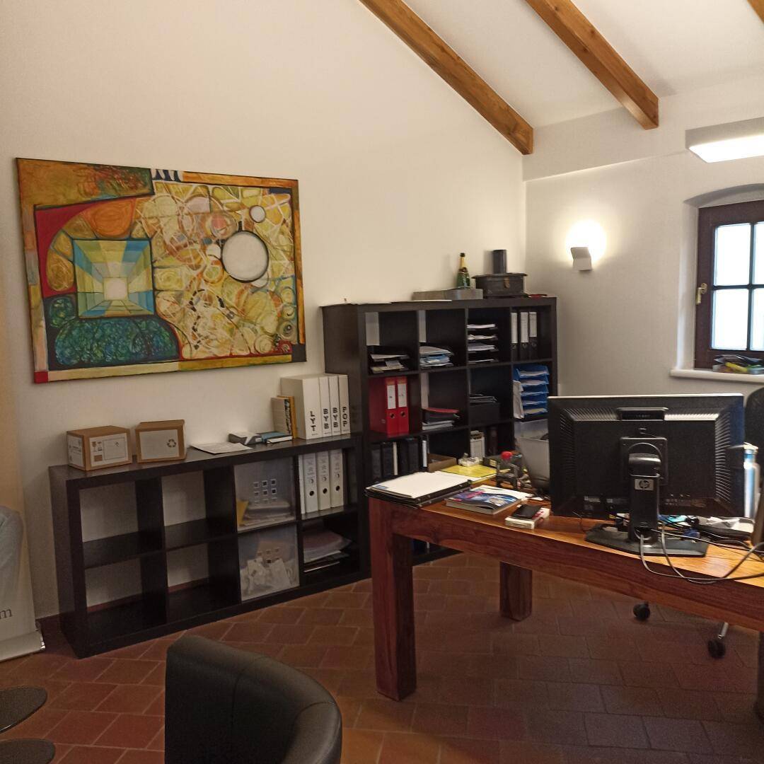 Geräumiges Büro mit Holzbalken, Terrakottafliesen und einem großen Schreibtisch mit Computer.
