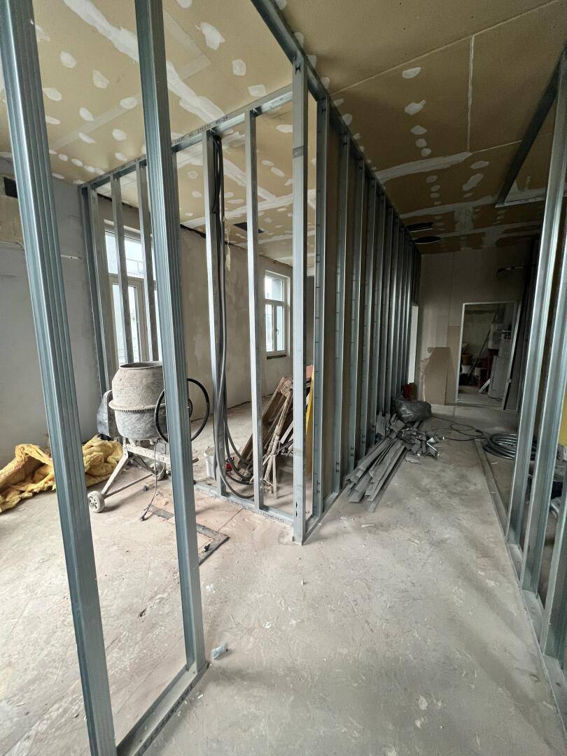 Innenraum im Rohbau mit Metallständern für Trockenbauwände und Baumaterialien auf dem Boden.