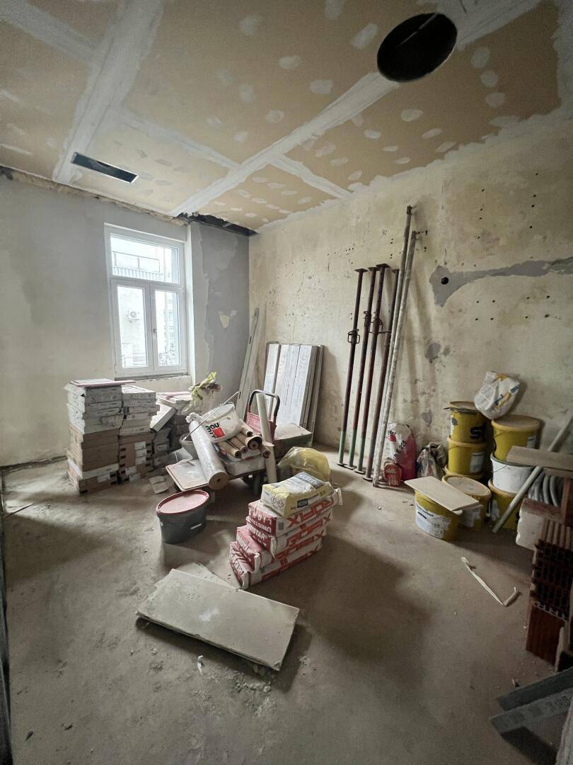 Raum im Rohzustand mit unverputzten Wänden, einem Fenster und gestapelten Baumaterialien.