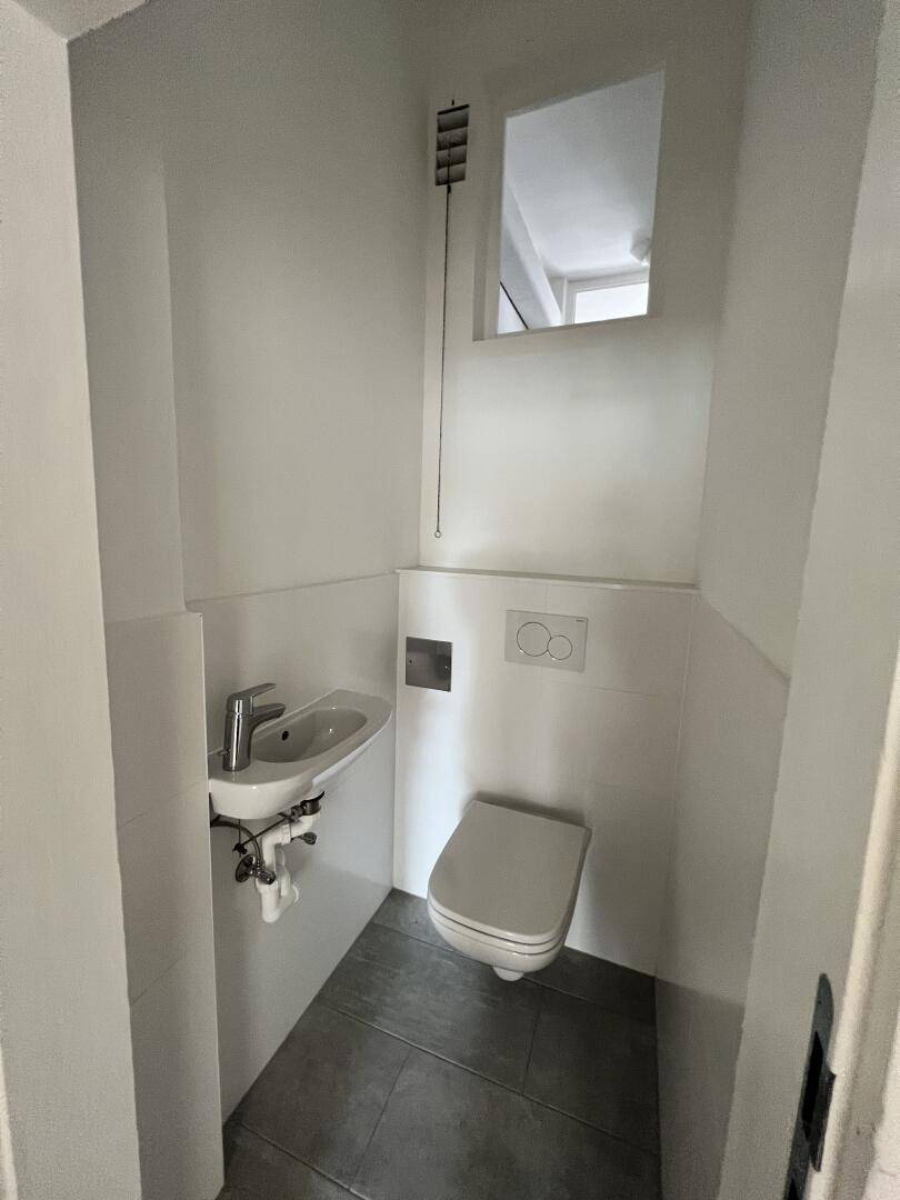 Kleines Gäste-WC mit wandhängendem WC, Waschbecken und einem kleinen Fenster für Belüftung.