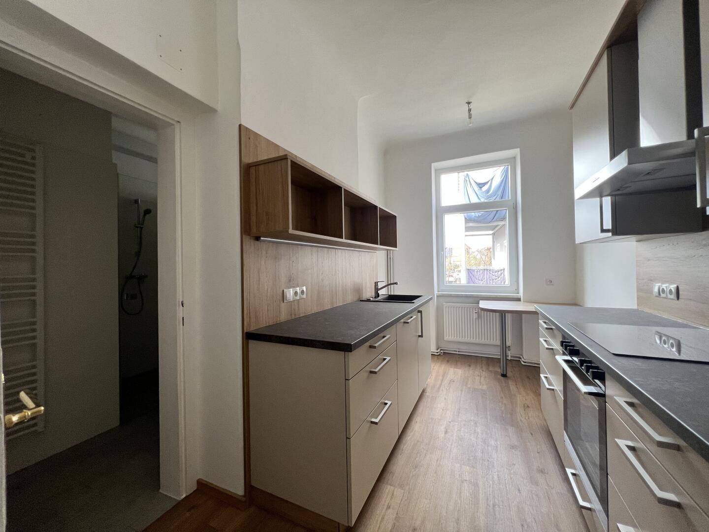 Neue Küche mit hellen Schränken, dunkler Arbeitsplatte und Blick in einen angrenzenden Raum.