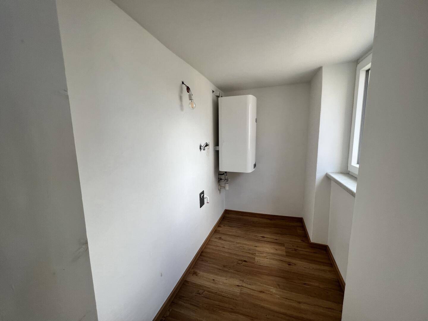 Praktischer Hauswirtschaftsraum mit Warmwasserbereiter und Fenster, ideal für Lagerung.