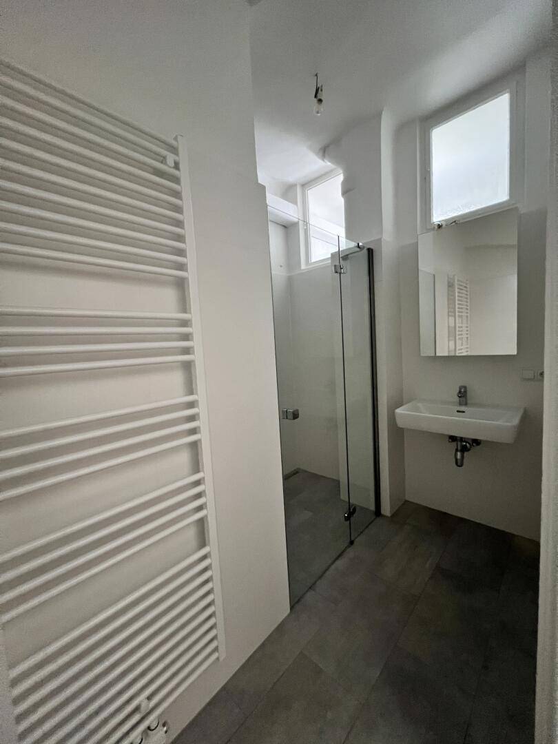 Modernes Badezimmer mit Duschkabine, Waschbecken, beheiztem Handtuchhalter und Fenster.