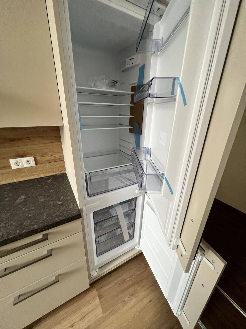 Offener Kühlschrank mit Gefrierfach, sauber und unbenutzt, integriert in die Küchenzeile.