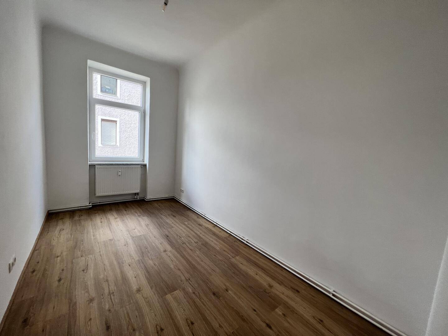 Helles Schlafzimmer mit Laminatboden und einem Fenster, bereit zur individuellen Gestaltung.