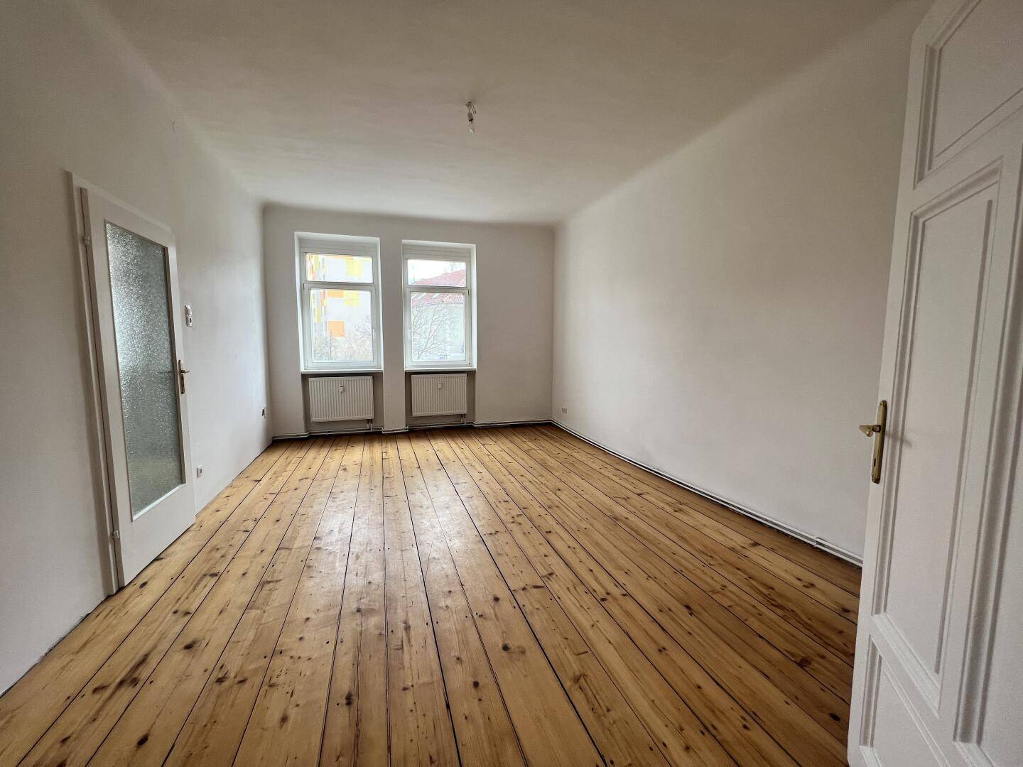 Helles Zimmer mit breiten Holzplankenboden und zwei Fenstern, bereit zur Einrichtung.