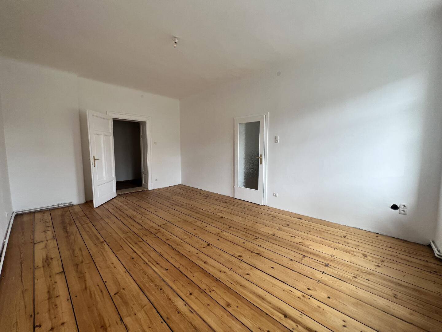 Geräumiger Raum mit breiten Holzplankenboden und mehreren Türen, vielseitig nutzbar.