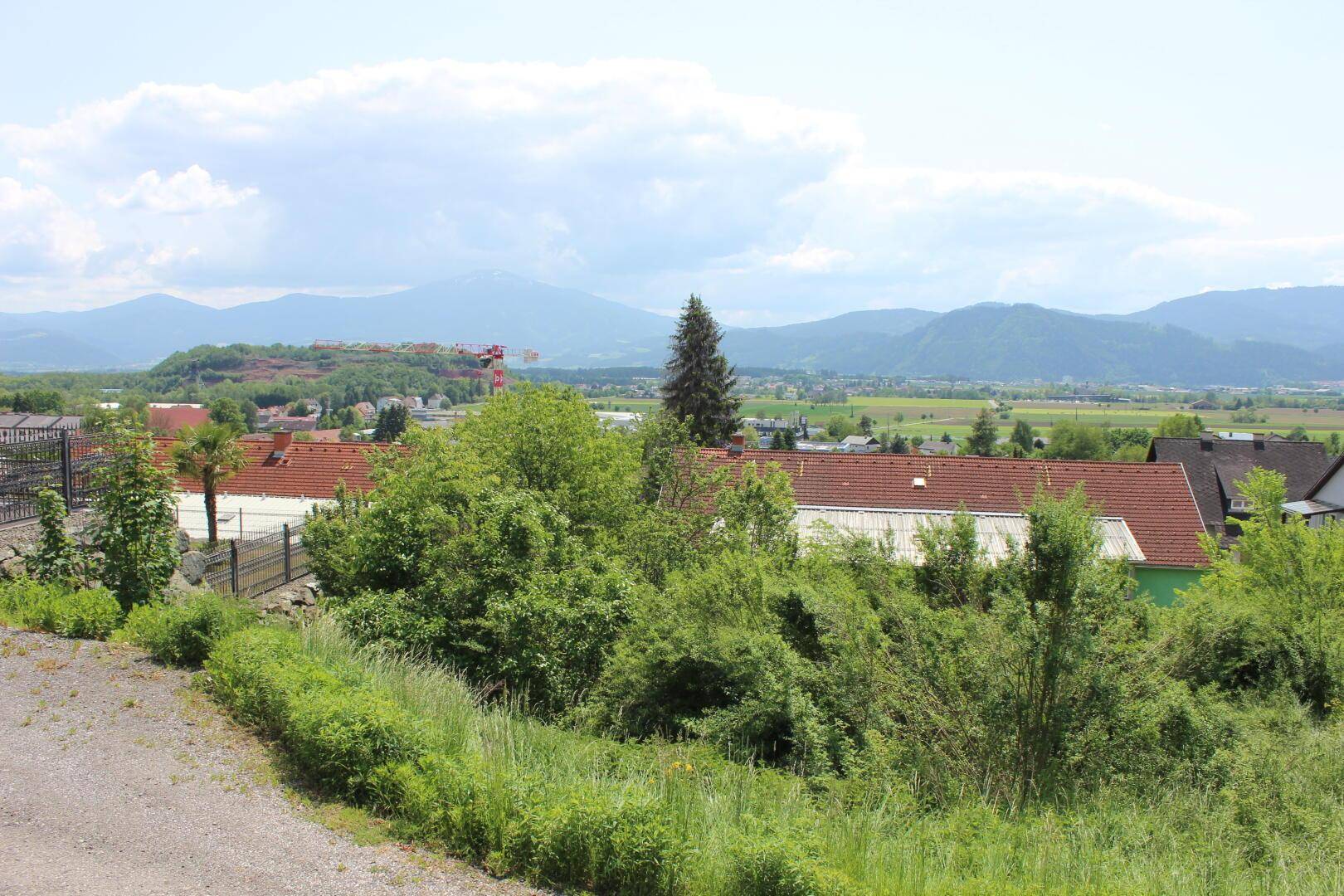 Panoramablick über eine Siedlung mit roten Dächern, grünen Feldern und einer Bergkulisse.