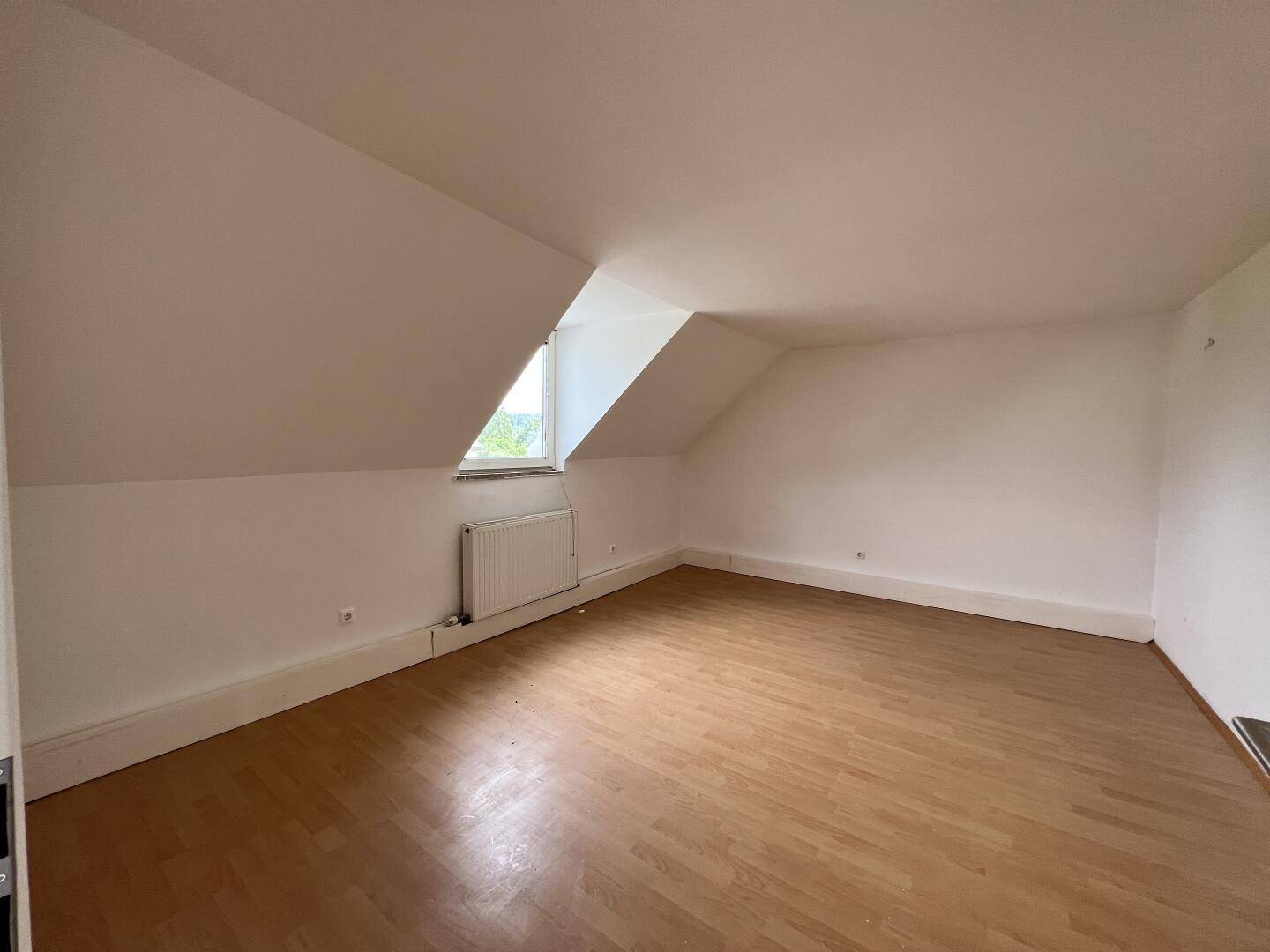 Geräumiger Dachbodenraum mit Laminatboden, schrägen Wänden und einem kleinen Fenster.