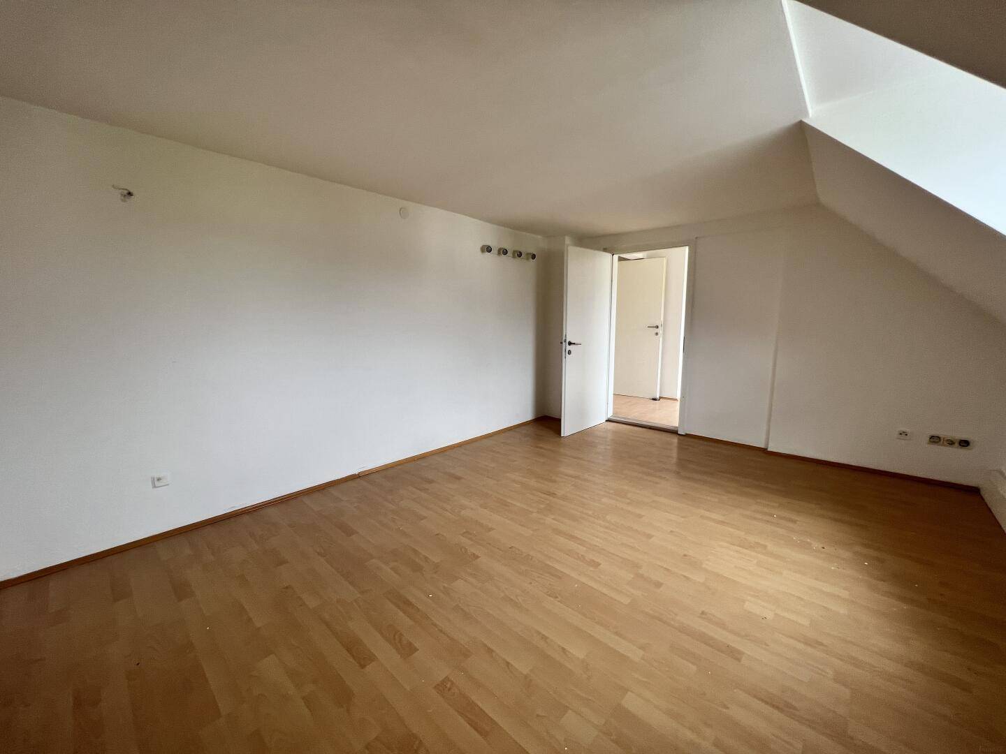 Heller Dachbodenraum mit Laminatboden und Zugang zu einem weiteren Zimmer.