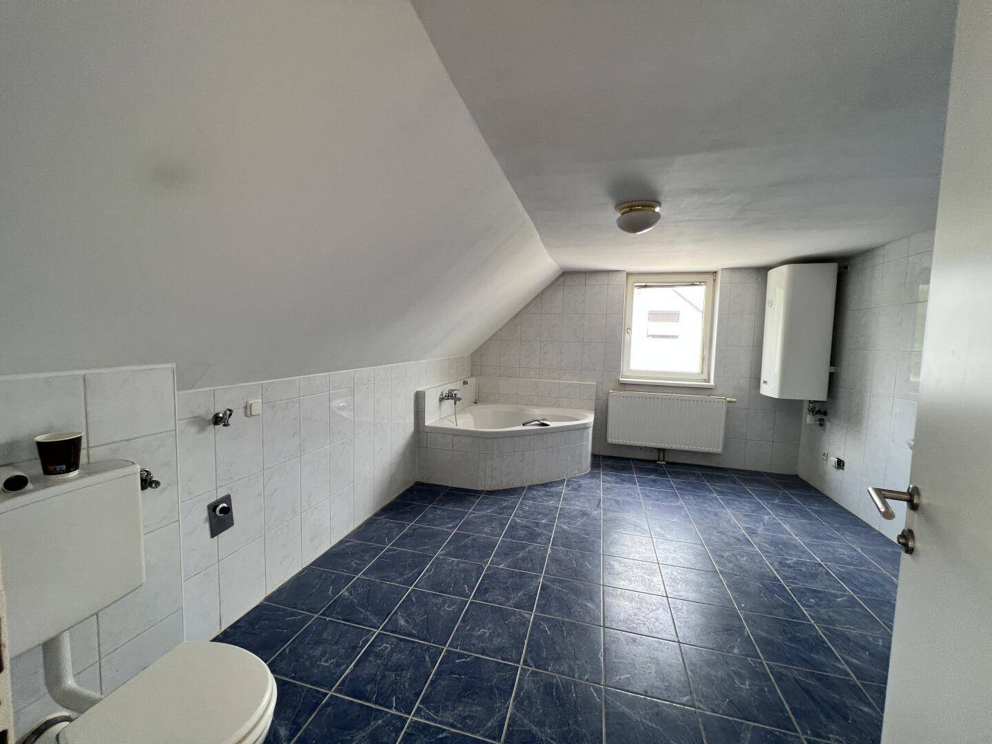 Geräumiges Badezimmer mit blauen Fliesen, Eckbadewanne, WC und Dachschräge.