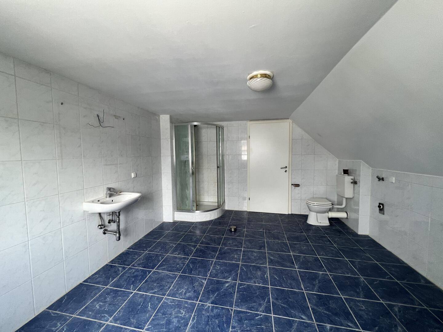 Badezimmer mit blauen Fliesen, Duschkabine, Waschbecken und WC unter der Dachschräge.