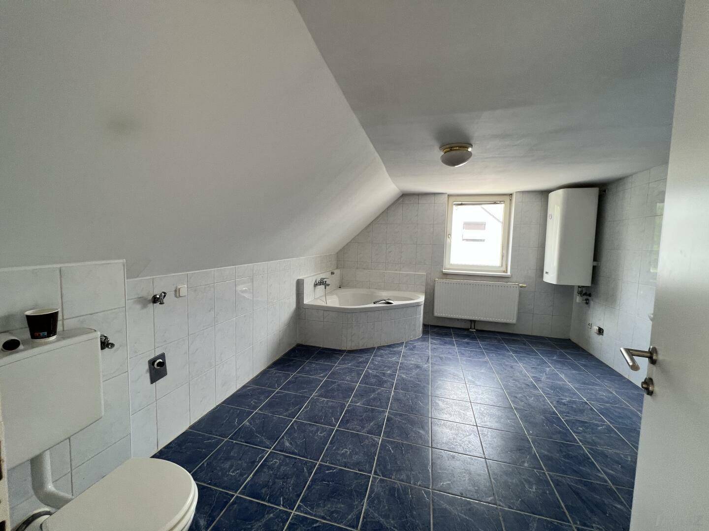 Geräumiges Badezimmer mit blauen Fliesen, Eckbadewanne und Dachschrägen im Obergeschoss.