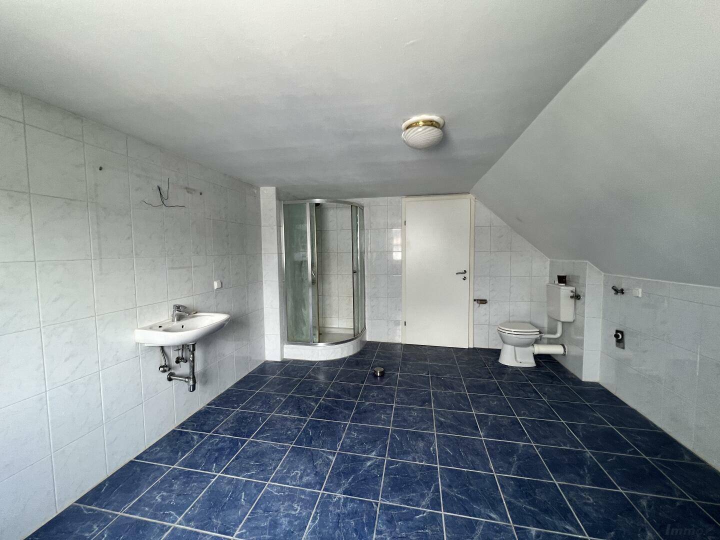 Großes Badezimmer mit Duschkabine, Waschbecken, WC und blauen Bodenfliesen im Dachgeschoss.