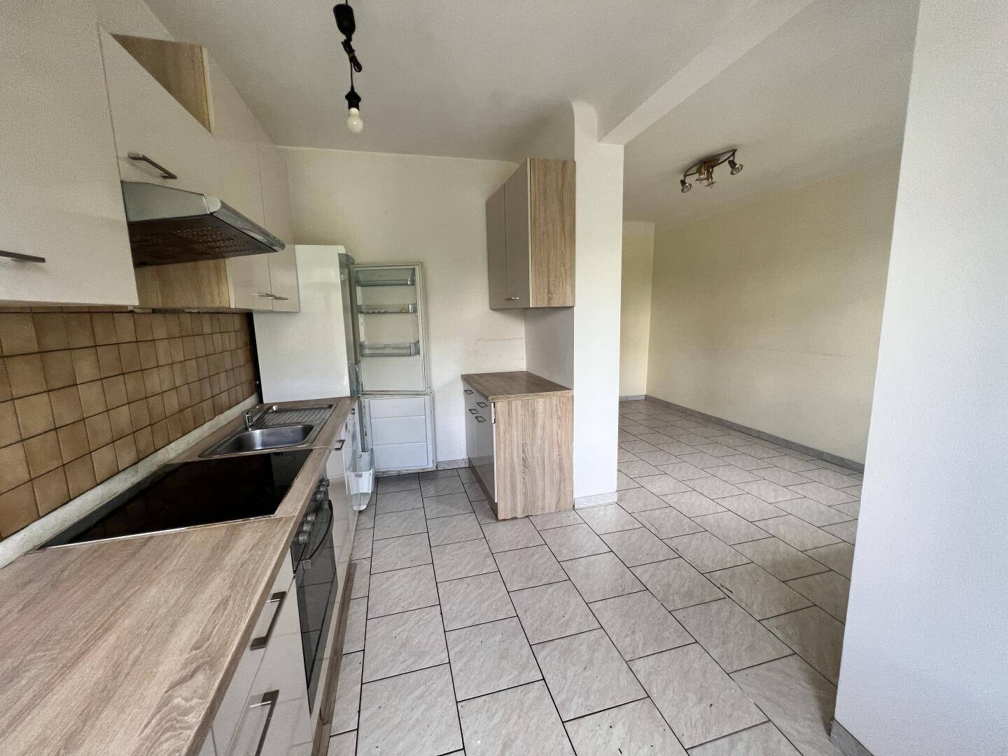Kleine Küche mit Einbauschränken, Holzoptik-Arbeitsplatten und Fliesenboden, offen zum Wohnbereich.