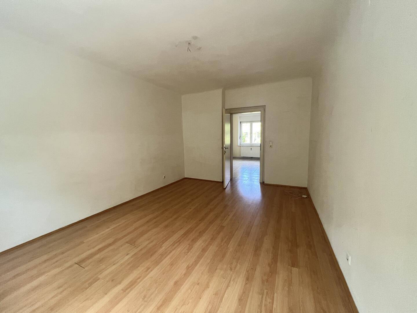 Geräumiges, leeres Wohnzimmer mit Parkettboden und Zugang zu einem weiteren Raum.