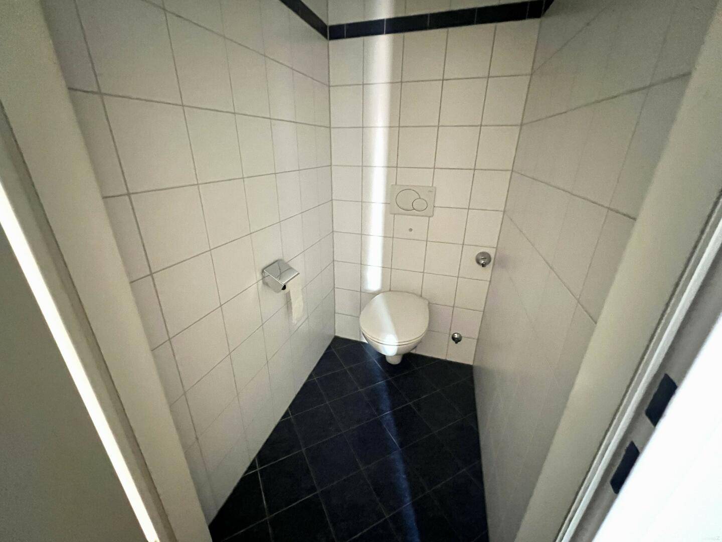 Separate Gästetoilette mit weißen Fliesen und dunklem Boden, praktisch für Besucher.