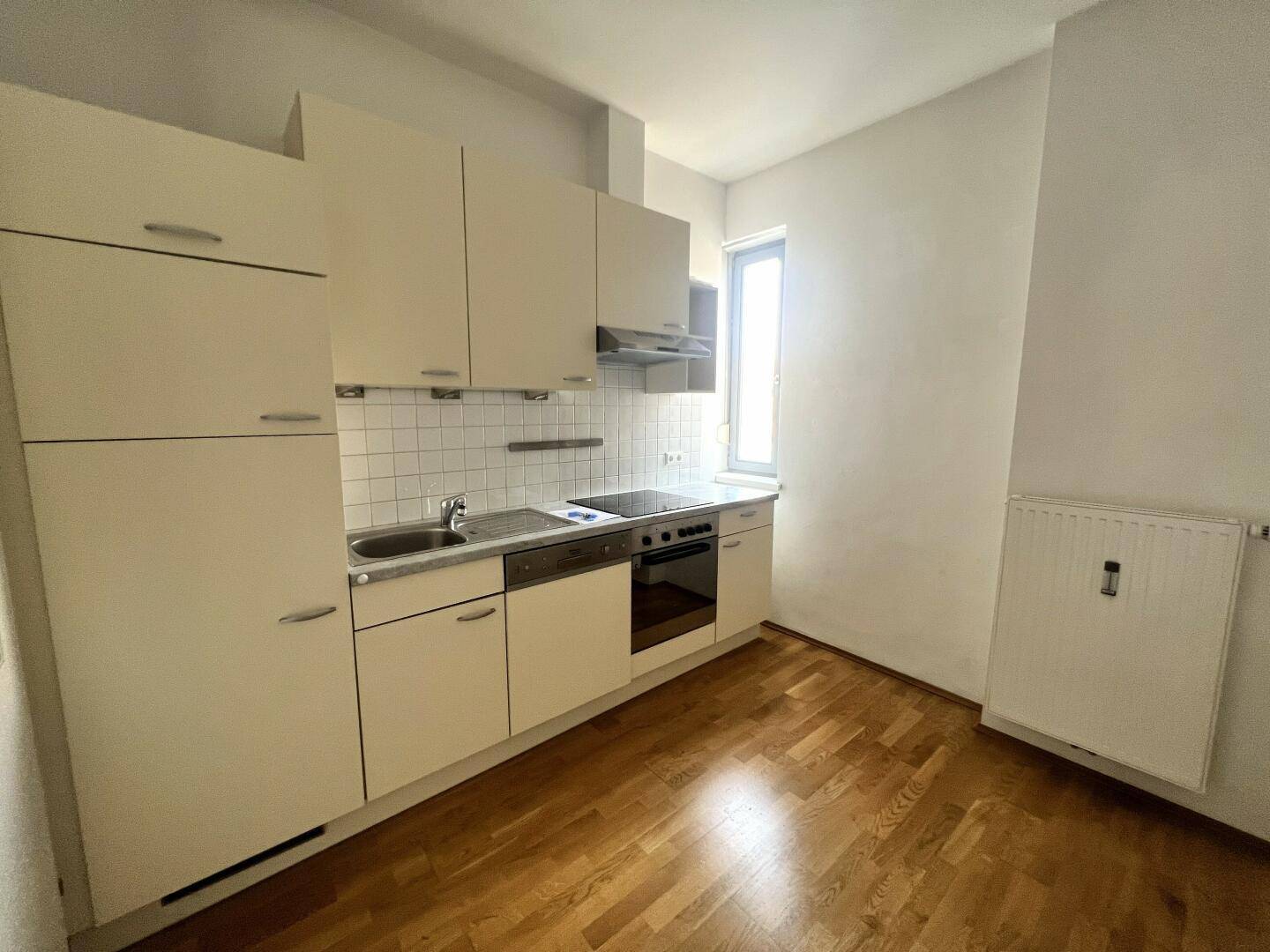 Kleine Einbauküche mit hellen Schränken, Spüle, Herd und Fenster für natürliche Belichtung.