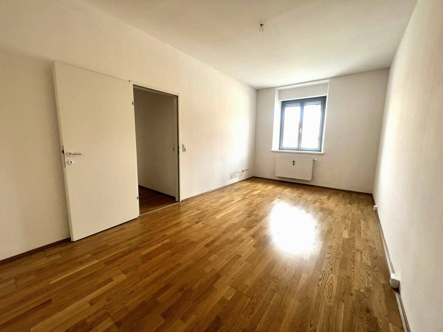 Heller, leerer Raum mit Parkettboden und Fenster, ideal als Wohn- oder Schlafzimmer.