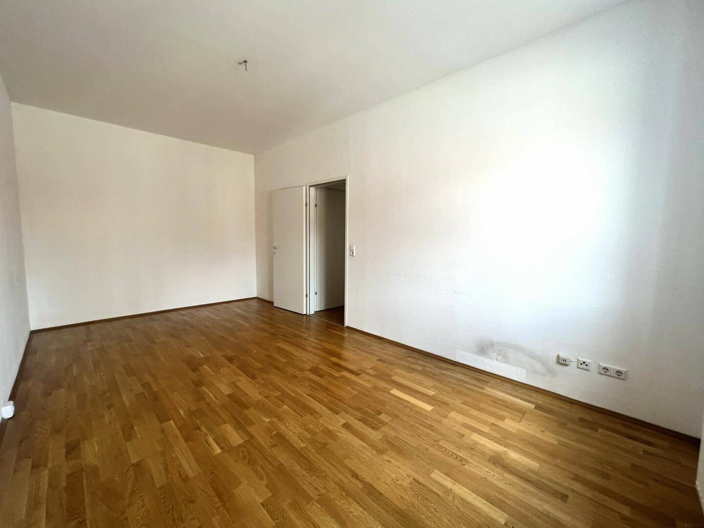 Leerer Wohnraum mit Parkettboden und weiß gestrichenen Wänden, bietet viel Gestaltungspotenzial.
