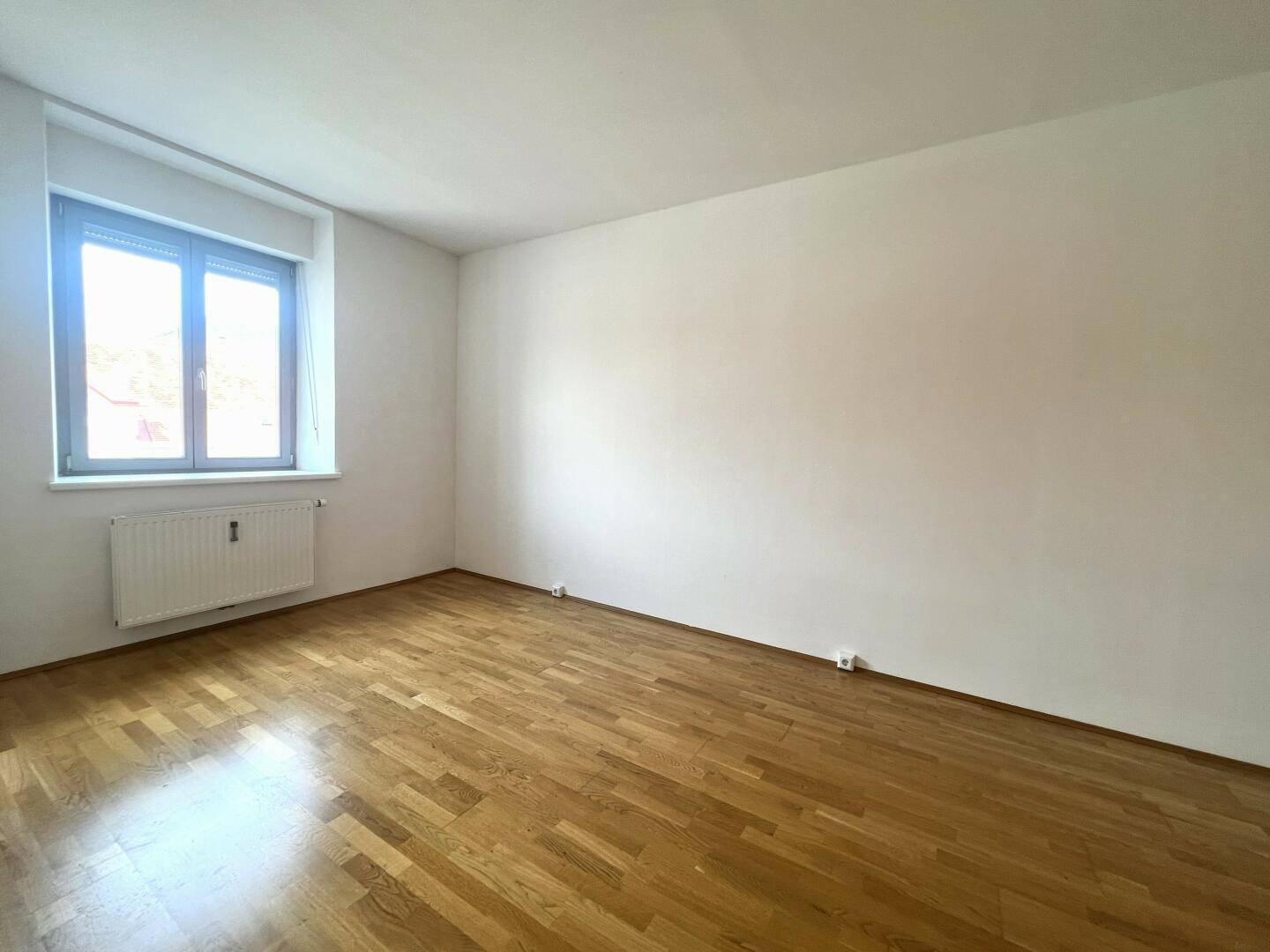 Geräumiger, heller Raum mit Holzparkett und großem Fenster, bereit zur individuellen Gestaltung.