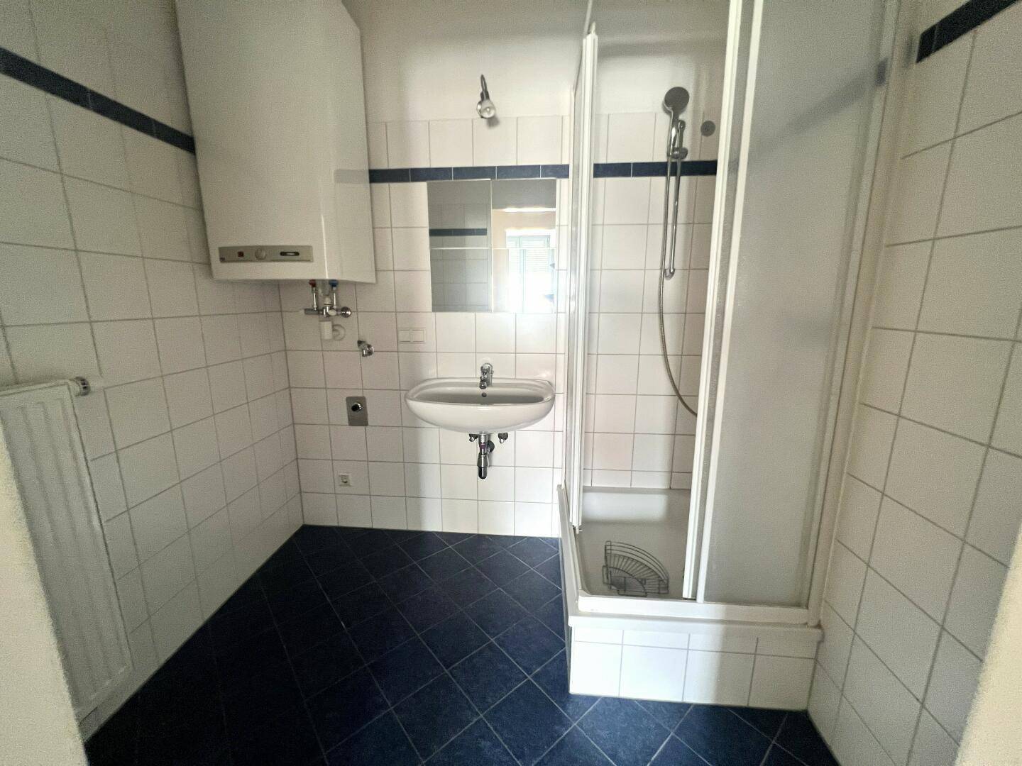 Badezimmer mit Dusche, Waschbecken und weißen Wandfliesen, funktional und hell.