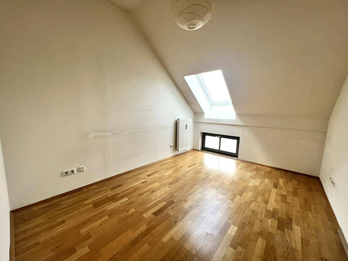 Gemütliches Schlafzimmer im Dachgeschoss mit Parkettboden, Dachfenster und Heizkörper.